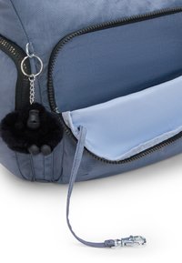 Zaino in nylon grigio con un portachiavi a forma di scimmia in peluche nera, dotato di una tasca con zip foderata di blu e un manico in tessuto grigio.