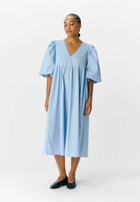 Une robe en coton bleu clair avec un décolleté en V plongeant et des manches courtes bouffantes, présentant une silhouette ample en A qui tombe sous le genou.