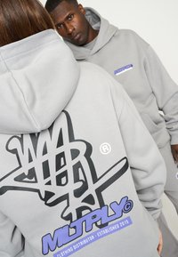 Graue Kapuzenpullover mit schwarzen Graffiti-ähnlichen Grafiken und blauen Texthighlights. Verfügt über Kordelzugkapuzen und einen lockeren Schnitt.