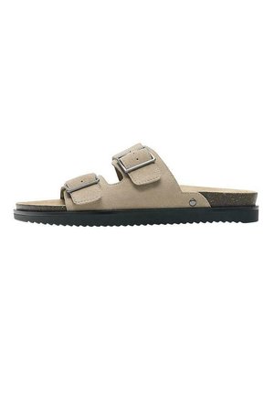 Beiger Wildleder-Slidesandale mit zwei verstellbaren Metall-Schnallenriemen und einer schwarzen, strukturierten Gummisohle.