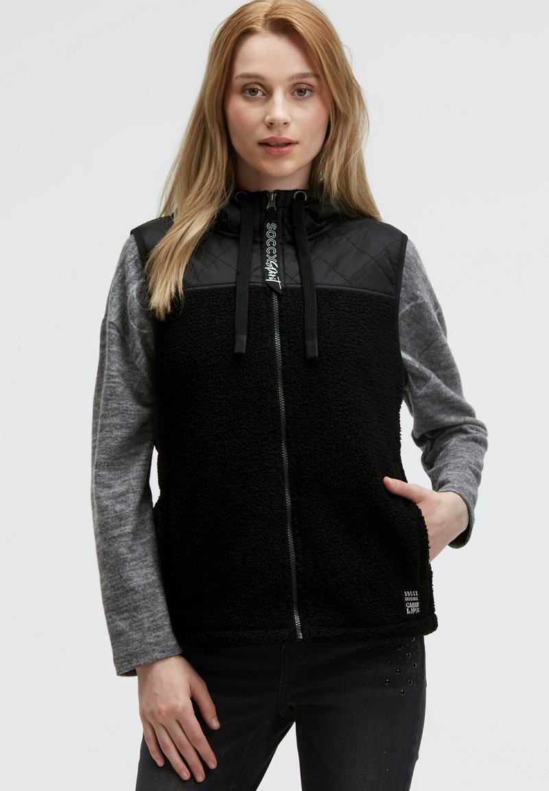 Schwarwest und graue Fleece-Weste mit einem gesteppte Oberteil, Reißverschluss, verstellbarer Kapuze und seitlichen Taschen. Auffälliges Logo am Kragen.