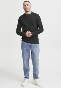 Mørk grønn ribbestrikket genser, rund halslinning, lange ermer, kombinert med lyseblå rette jeans og hvite sneakers med gulldetaljer.