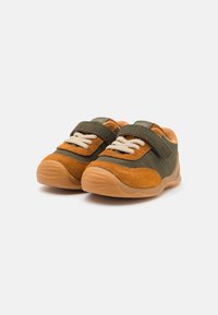Scarpe verdi e arancioni con tomaia in suede e tessuto, dotate di una fascia in Velcro e lacci beige, montate su una suola in gomma flessibile.