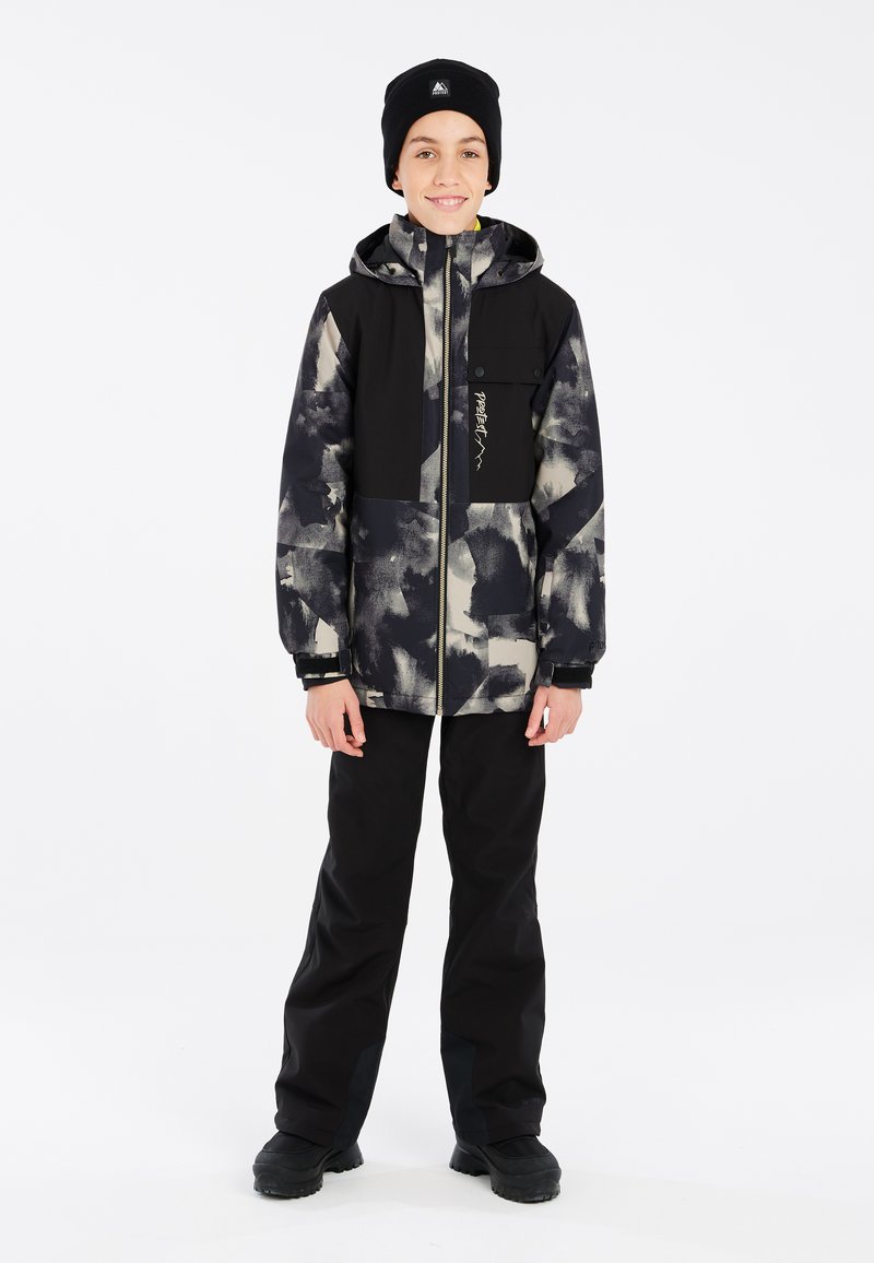 Schwarze und graue Winterjacke mit abstrakten Mustern, Reißverschluss und zwei Taschen, kombiniert mit schwarzen, wasserdichten Hosen und Stiefeln.