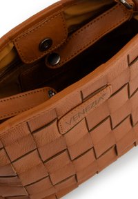 Sac en cuir brun avec une texture tissée et des accents lisses. Il dispose d'une fermeture à pression, d'un logo embossé et d'un intérieur doublé de tissu.