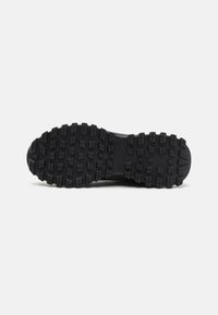 Black trail shoe outsole featuring deep, multi-directional treads for traction and durability. Made of rubber with a textured finish.