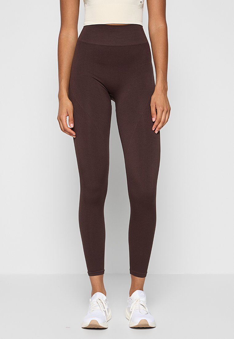 Brązowe leggings z wysokim stanem, z teksturowanym wzorem i bezszwowym designem, w zestawie z białymi trampkami. Wykonane z rozciągliwej, oddychającej tkaniny.