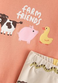 Ροζ βαμβακερό τοπ με το κείμενο «FARM FRIENDS», που απεικονίζει σκίτσα αγελάδας, χοίρου και πάπιας. Κρεμ σορτς με ζώνη μέσης με σχέδιο φιδιού.