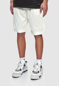 Lysecreme atletiske shorts med struktureret stof, opsmøgede sømme og broderet logo. Matchet med hvide og sorte sneakers.