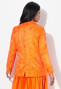 Blazer naranja con un estampado de leopardo texturizado, mangas largas y puños abotonados. Detalle de apertura en la espalda que mejora el movimiento y el ajuste.
