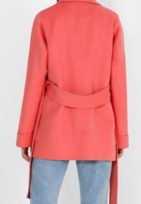 Abrigo coral de mezcla de lana con cintura ceñida, puños anchos y cuello de solapa, con una textura suave y un diseño entallado.