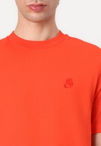 Majica s kratkimi rokavi v svetlo oranžni barvi, izdelana iz gladkega bombaža. Ima majhen, tonalen vezen logo na prsih. Okrogla izreza.