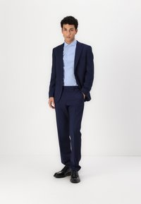 Navy suit with a fitted blazer and matching trousers, paired with a light blue shirt and black dress shoes. Clean lines and smooth texture.