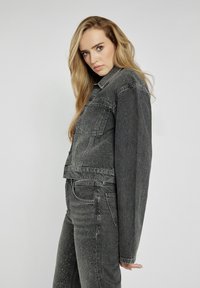 Skórzana kurtka z czarnego denimu z zapięciem na guziki, przednimi kieszeniami i detalami. Połączona z dopasowanymi dżinsami z ćwiekami.