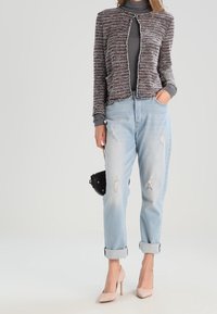 Veste courte tricotée multicolore avec col rond, associée à un jean bleu clair déchiré et des talons rose pâle.