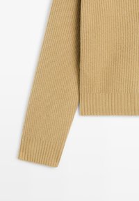 Maglione beige lavorato a maglia con polsini e orlo a costine, caratterizzato da tessuto strutturato e una vestibilità casual, con un focus su calore e comfort.