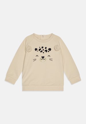 Sudadera beige con mangas largas, que presenta un diseño de cara de animal juguetona en negro y dorado. Tejido suave con bordes redondeados.