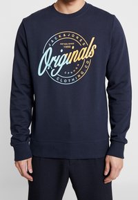 Mörkblå crewneck-tröja i bomull med en cirkulär logotyp framtill med orange och ljusblå text "Jack & Jones Originals".