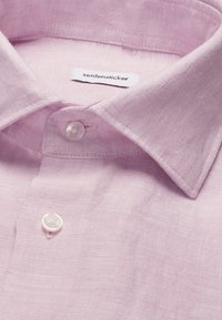 Chemise en lin rose clair avec col pointu, deux boutons blancs visibles et une étiquette de marque "seidensticker" à l'intérieur du col.