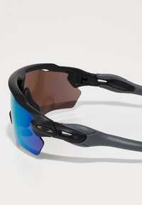Sportowe okulary przeciwsłoneczne z szarym korpusem, soczewkami w niebiesko-zielonym gradiencie oraz regulowanymi noskami. Smukły design z wbudowanymi zawiasami dla lepszego komfortu.