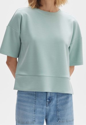 Mujer con una blusa de manga corta color azul claro con bajo asimétrico combinada con unos vaqueros azules de lavado medio con bolsillos parche delanteros.