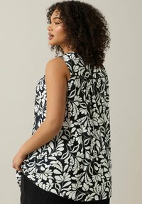 Svart ärmlös topp med ett vitt blommönster, något rundad nederkant och textil med struktur, vilket ger ett lätt och luftigt utseende.