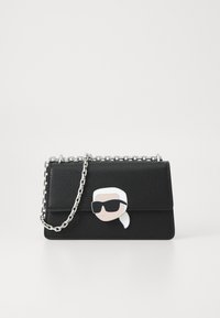 Fekete bőr kézitáska texturált felülettel, ezüstlánc pánttal és napszemüveget viselő mesefigurával a felső részén.