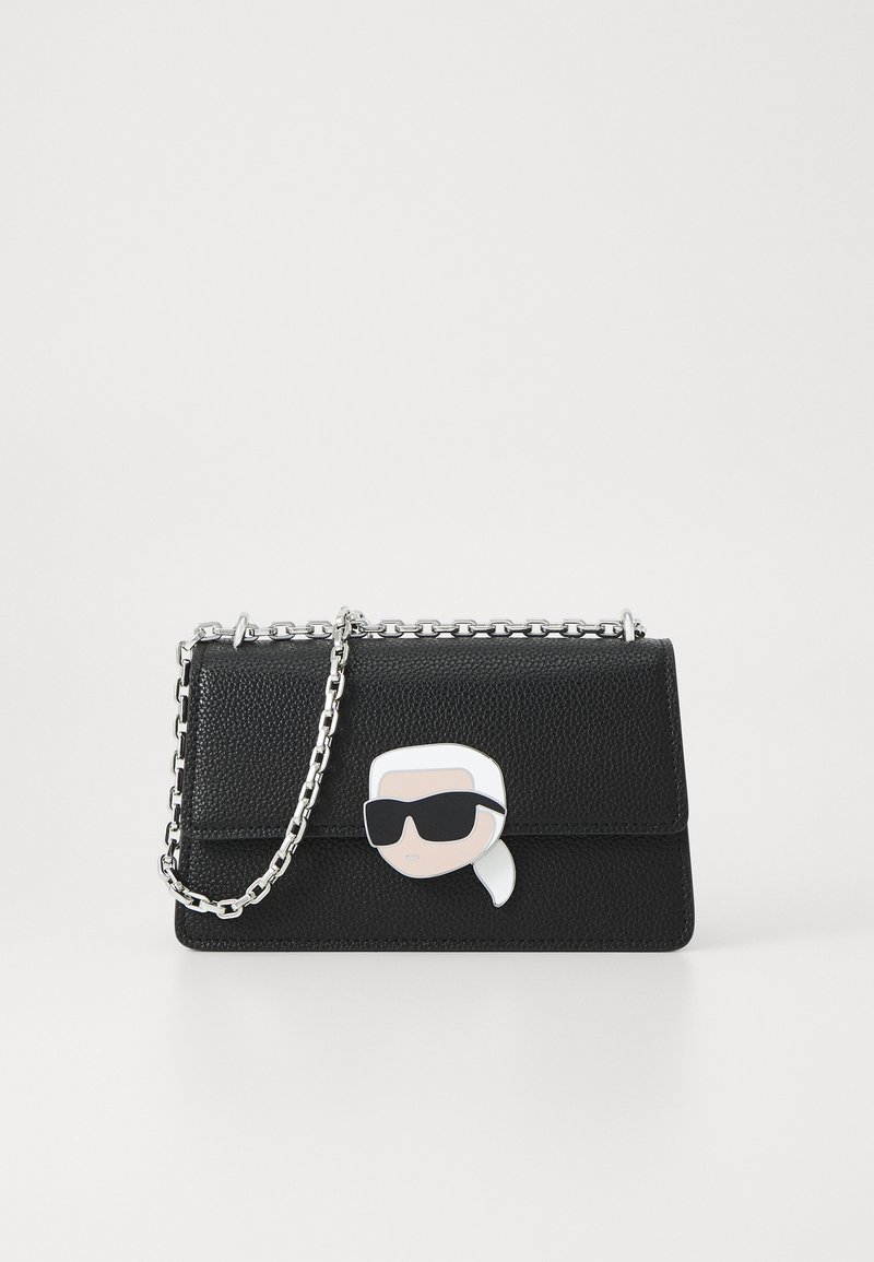 Fekete bőr kézitáska texturált felülettel, ezüstlánc pánttal és napszemüveget viselő mesefigurával a felső részén.