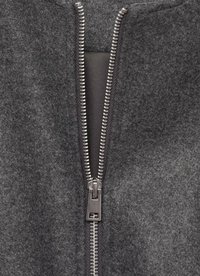 Garment grigio in feltro con una zip metallica prominente, che mostra una texture liscia e un design elegante. I denti della zip sono visibilmente allineati e metallici.