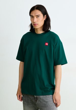Tumši zaļš kokvilnas T-krekls ar īsām piedurknēm un apaļu kakla izgriezumu. Ar mazu sarkanu logo uzlīmi kreisajā krūtī. Brīvs griezums.