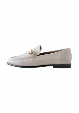 Mocasín de piel beige con punta redonda, con un detalle de hardware en tono dorado en la parte superior y una suela de goma negra.