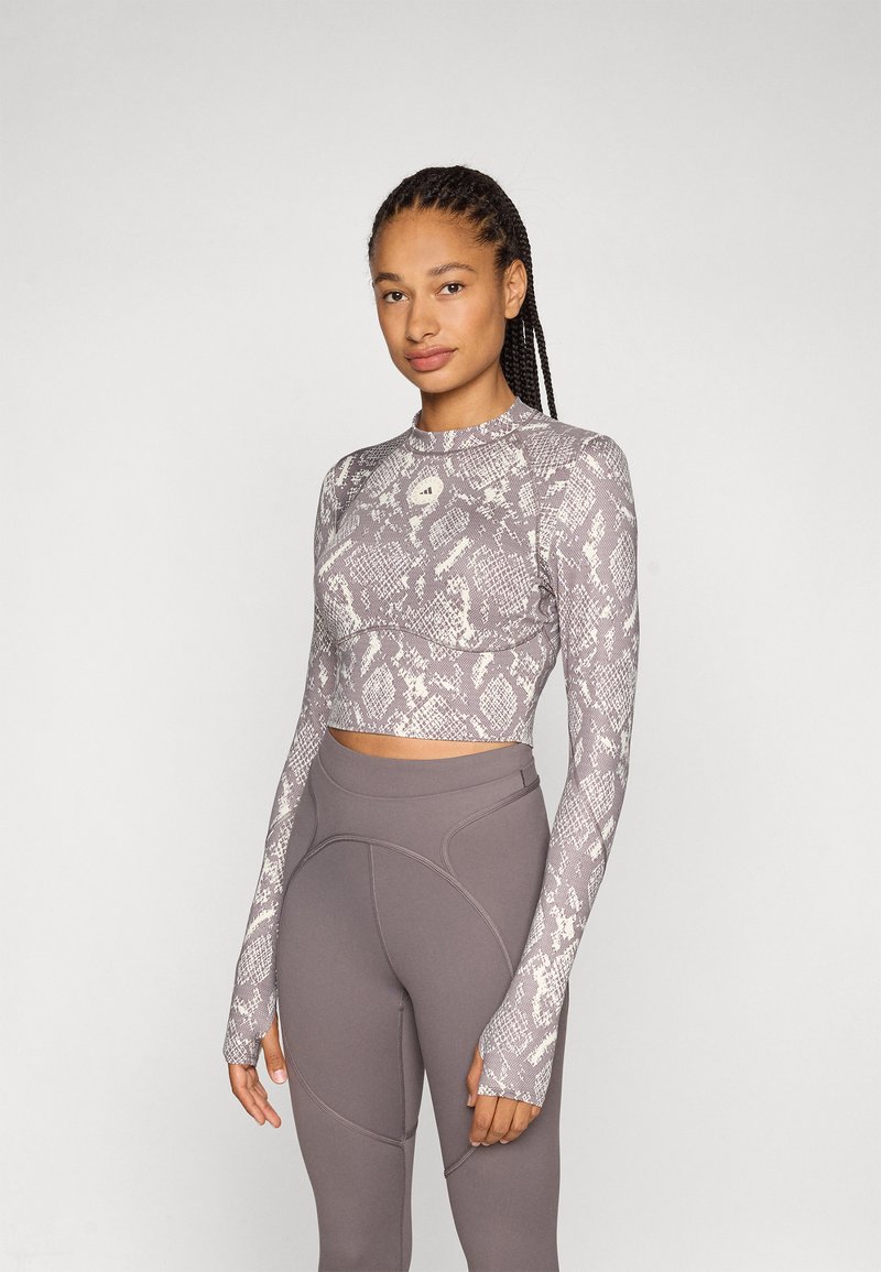 Grå slangeskinnmønstrete langermet crop topp med tettsittende design og hull for tommelen, kombinert med høyhårede grå leggings med sømdetaljer.