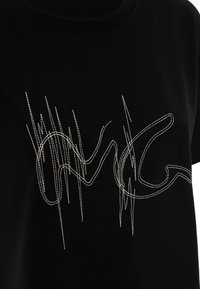 T-shirt noir avec un col rond présentant des lignes et des motifs brodés blancs complexes sur le devant. Tissu en coton doux.