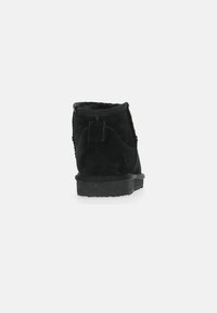 Zwarte suède enkelboot met een gladde textuur, ronde bovenkant en platte rubberen zool. Voorzien van een klein trekflapje aan de achterkant voor gemakkelijk aan- en uittrekken.
