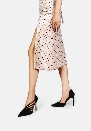 Décolleté nere in suede con punta appuntita e design con cinturini. Indossate con una gonna in satin rosa a pois con uno spacco laterale.