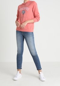 Růžová mikina s logem "Abercrombie", klokaní kapsou a žebrovanými manžetami. V kombinaci s světle modrými džínami a bílými teniskami. Jednoduchý design.