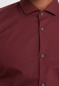 Bordeaux knoopshirt met een gladde textuur, puntige kraag en zwarte knopen. Heeft een slim fit en minimale stiksel-details.
