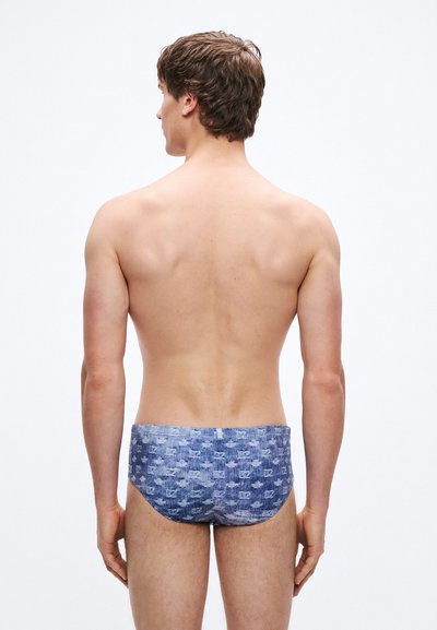 Bañador tipo slip con un patrón pixelado en azul y azul claro, confeccionado con tela elástica, de corte bajo y textura suave.
