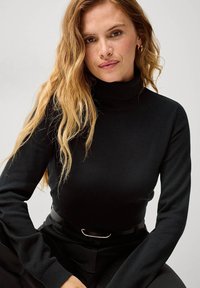 Maglione a collo alto di colore nero con una texture a coste, dotato di maniche lunghe e un design aderente. Tessuto liscio con accenti minimi.