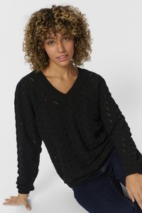 Maglione nero a maglia con scollo a V, maniche lunghe e un motivo ad apertura. Le finiture a coste sui polsini e sull'orlo aggiungono texture. Indossato sopra jeans scuri.