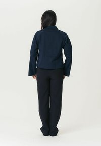 Tumši zila jaka ar apkakles apkakli un garām piedurknēm, ar strukturētu dizainu un nedaudz saīsinātu siluetu. Kombinēta ar melniem biksēm.