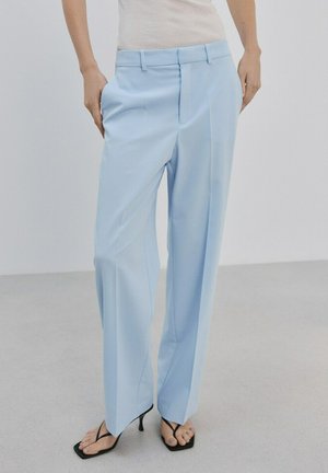 Mujer con pantalones anchos de pierna ancha a medida de color azul claro, top sin mangas blanco de canalé y sandalias negras de tacón con tiras delgadas.