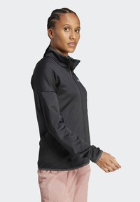Crna zip-up jakna s visokim ovratnikom, dugim rukavima i teksturiranom tkaninom. Ima logo na prsima i kontrastne šavove.