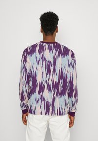 Chemise à manches longues présentant un motif abstrait violet, bleu et rose. Fabriquée dans un tissu doux avec des poignets et un col côtelés.