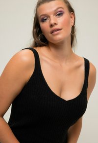 Zwarte geribbelde gebreide tanktop met een diepe V-hals en brede schouderbanden. Heeft een zachte textuur en een aansluitende snit.