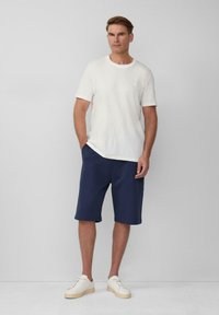 Witte t-shirt met korte mouwen van textuurstof, gecombineerd met marineblauwe kniebrede shorts en crèmekleurige sneakers. Eenvoudig ontwerp en pasvorm.