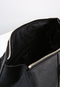 Czarna torebka skórzana o fakturze z złotym zamkiem, pokazująca pustą wnętrze wyłożone materiałem z logo oraz wieloma kieszonkami na karty.