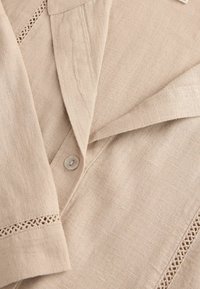 Beige Leinenhemd mit einem Kragen, einem einzelnen Knopfverschluss und zarter Spitze an den Ärmeln für zusätzlichen Stil und Textur.