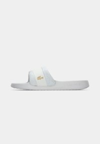 Σανδάλι slide σε ανοιχτό γκρι και λευκό, με υφασμένο λουρί και χρυσό λογότυπο Lacoste. Ίσια σόλα με ελάχιστες λεπτομέρειες σχεδίασης.