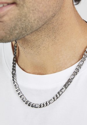 Silberne Halskette aus Edelstahl mit ineinandergreifenden Gliedern, getragen über einem weißen T-Shirt. Zeigt eine glatte, glänzende Oberfläche.